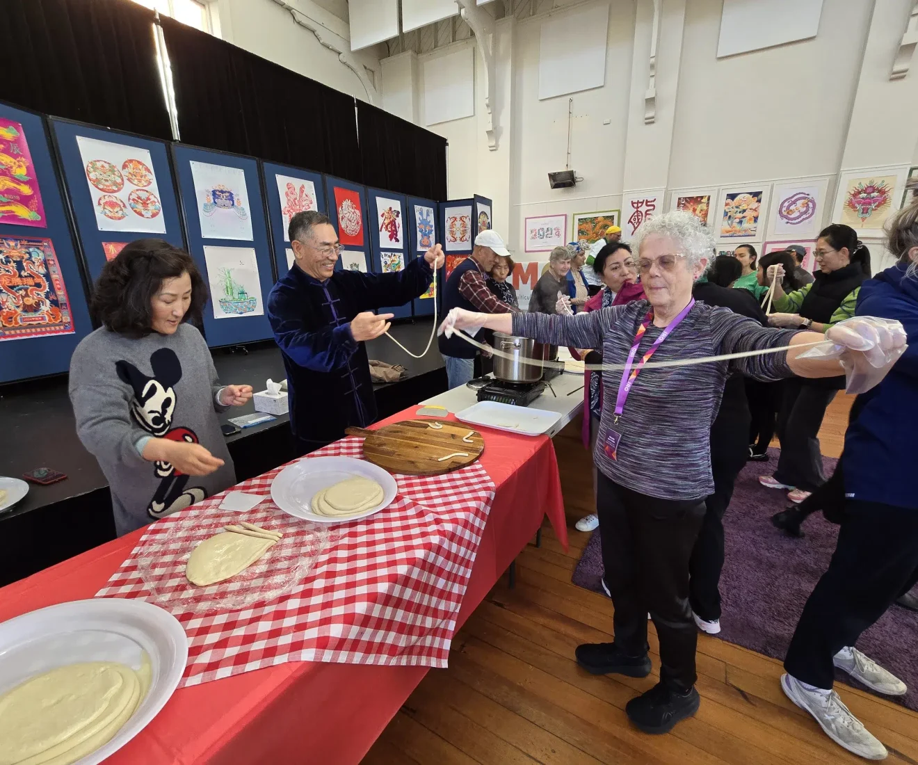 People making noodles at cultural event indoors.