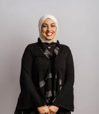 Smiling person wearing a hijab and black outfit.
