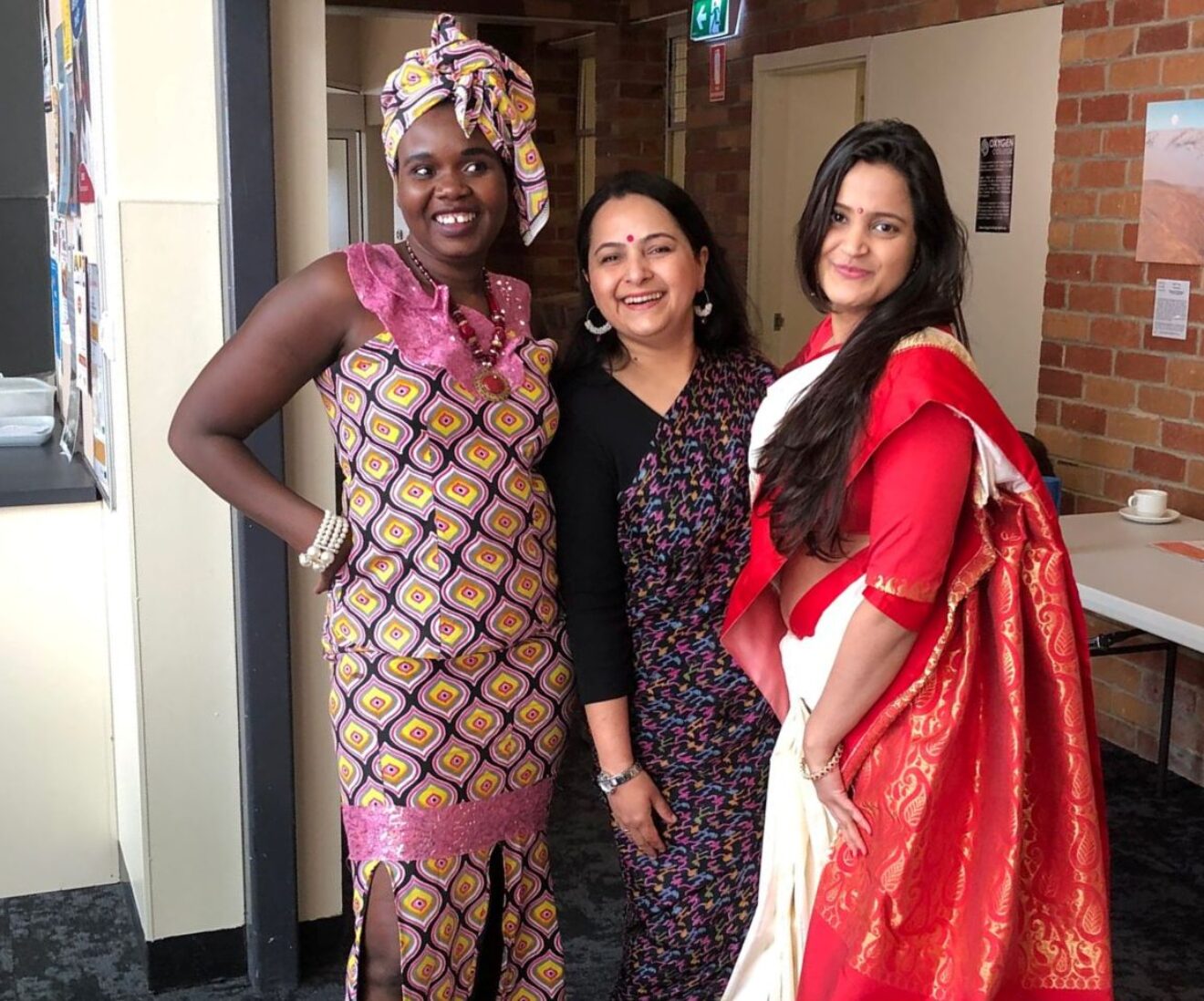 Three women in colourful cultural attire smiling together.