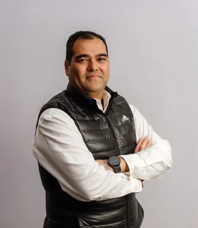 Man in black vest crosses arms, smiling.