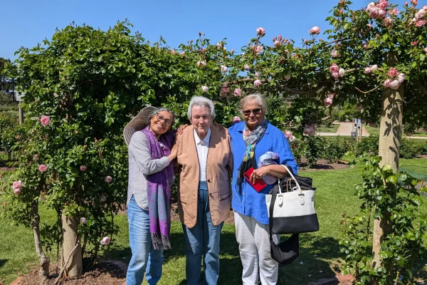 Three adults smiling in garden under rose arch.
